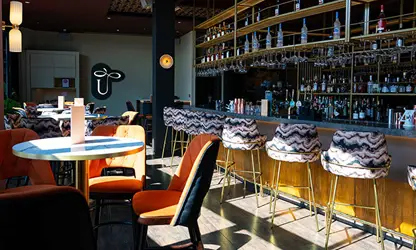 Stylish bar and restaurant interior with a long illuminated bar, colorful chairs, and tables.