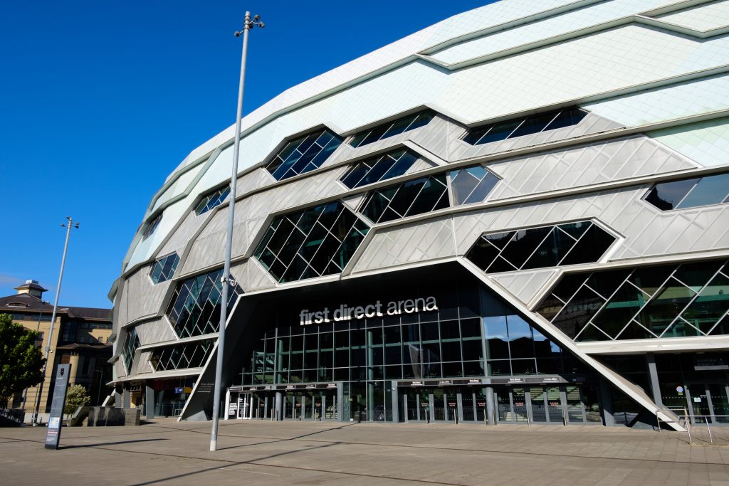 First Direct Arena in Leeds, showing its distinctive white geometric hexagonal facade under a clear blue sky.